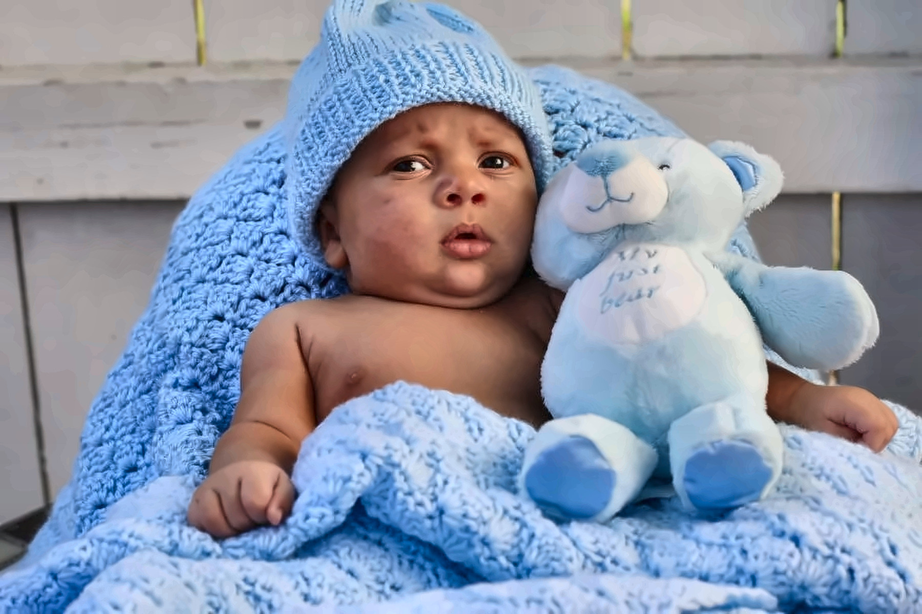 Newborn resting on a blue blanket beside a teddy bear